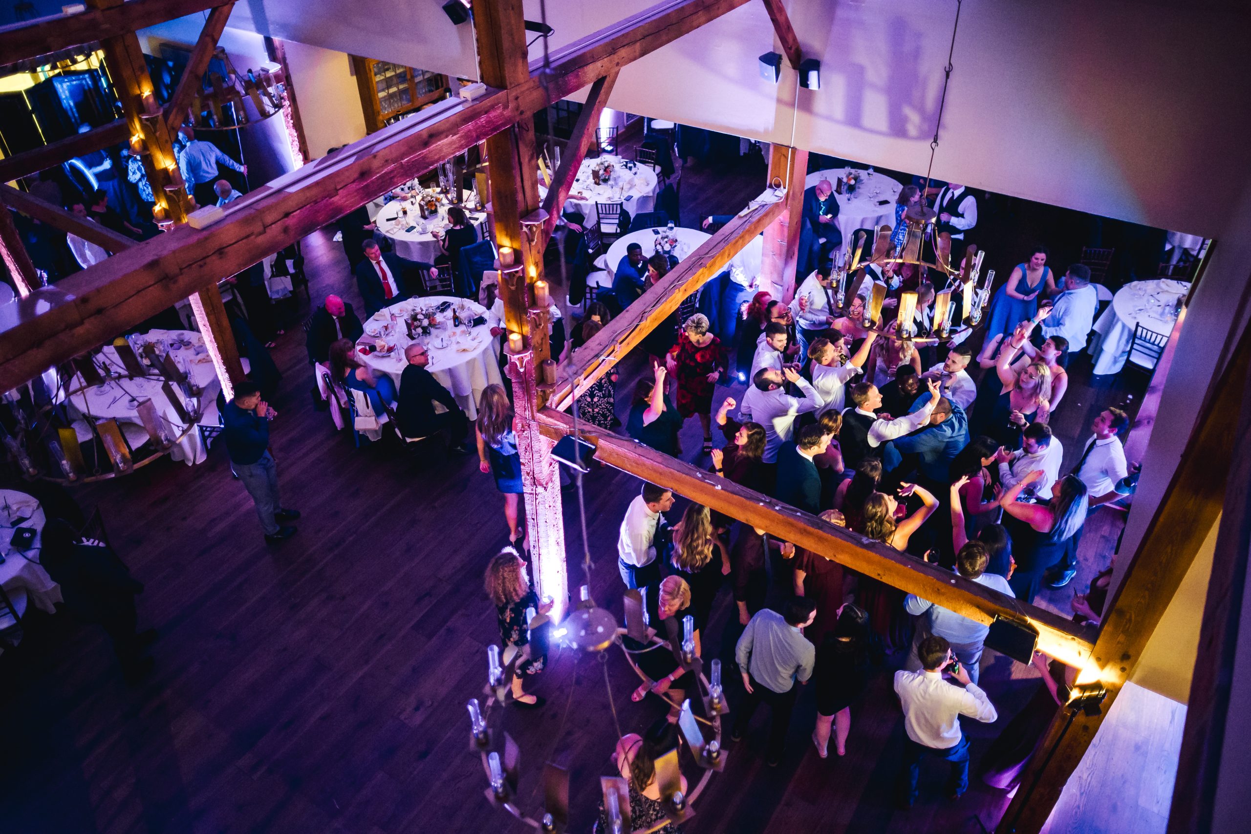 Wedding guests dancing in a timber-framed venue with purple uplighting